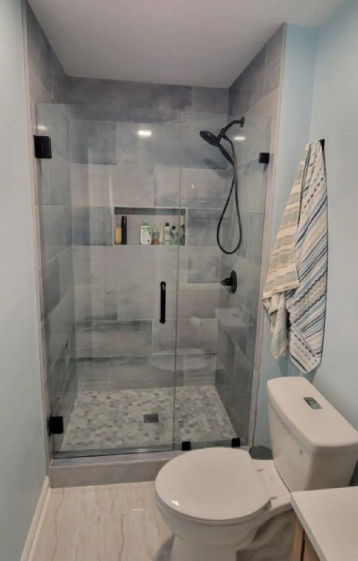 Compact glass shower with dark tile flooring and matte black hardware