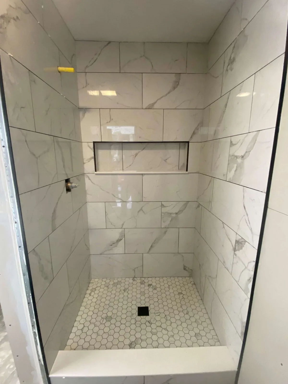 Tile shower remodel with white marble surround, built-in niche, and gold hardware