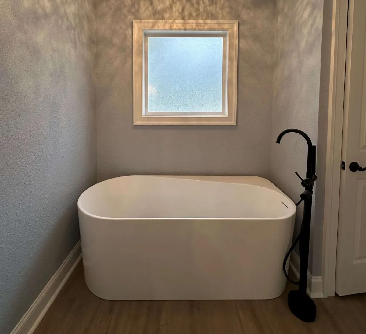 Sculptural freestanding tub installed beneath frosted privacy window