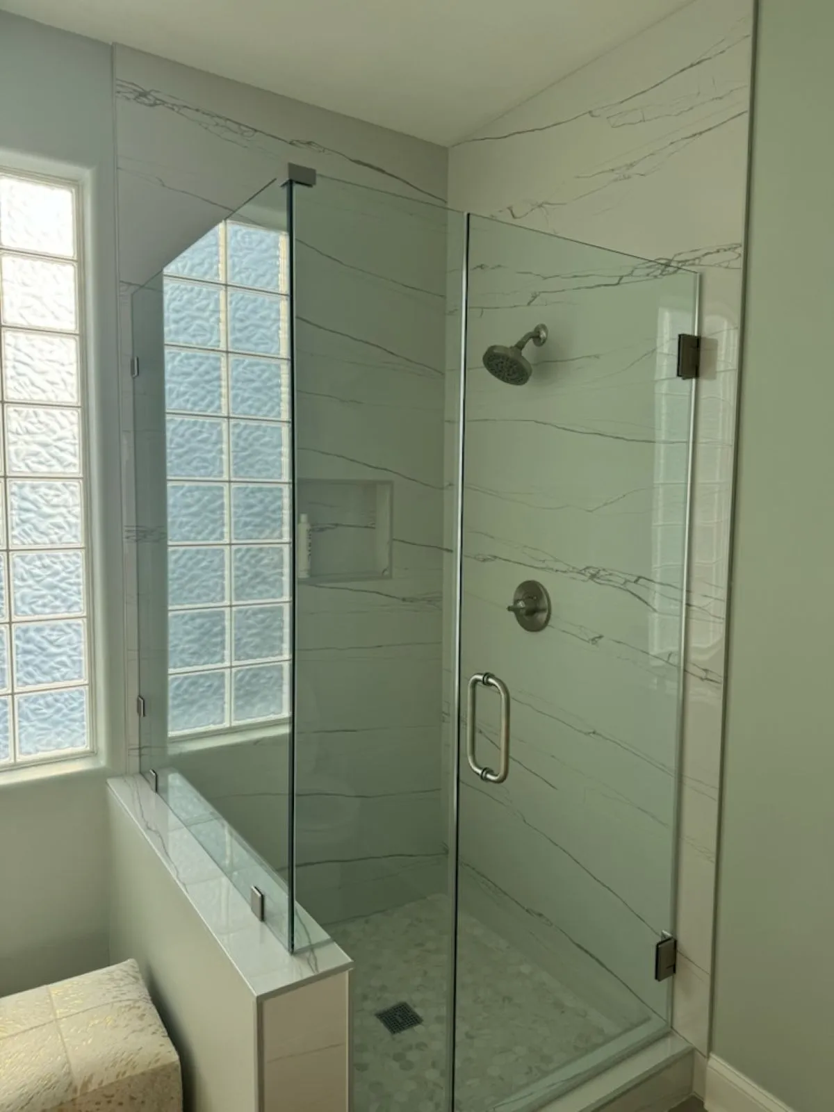 Walk-in shower with large tile walls, built-in shelf, and frameless glass door.