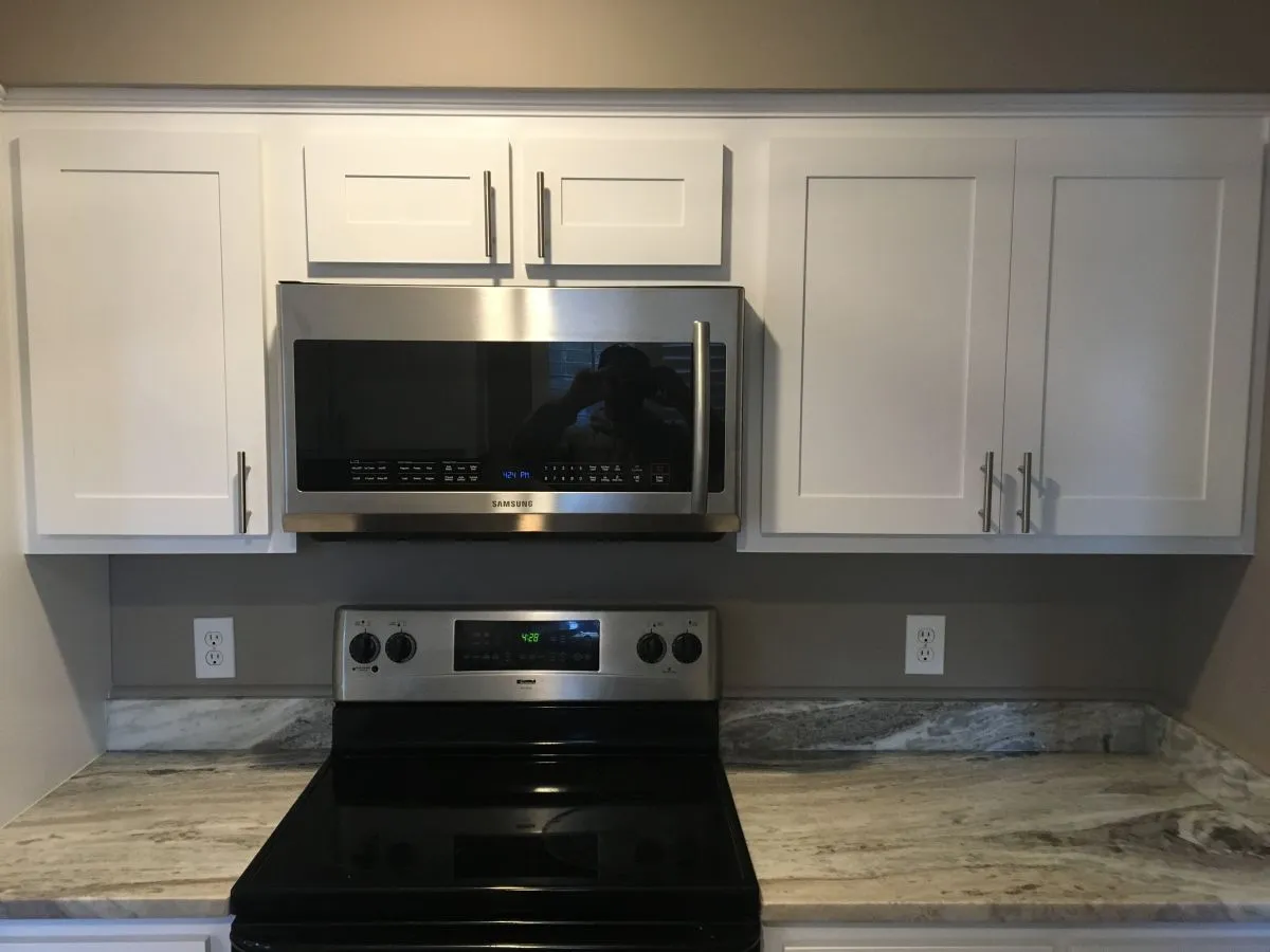 White upper cabinets with crown molding and over-range microwave installed in remodeled kitchen