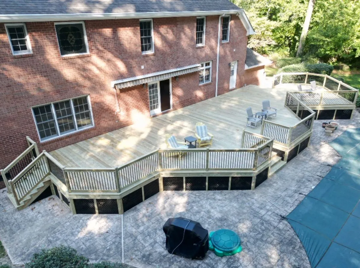 Expansive multi-section wood deck built behind a red brick home in Norfolk with railing and pool access