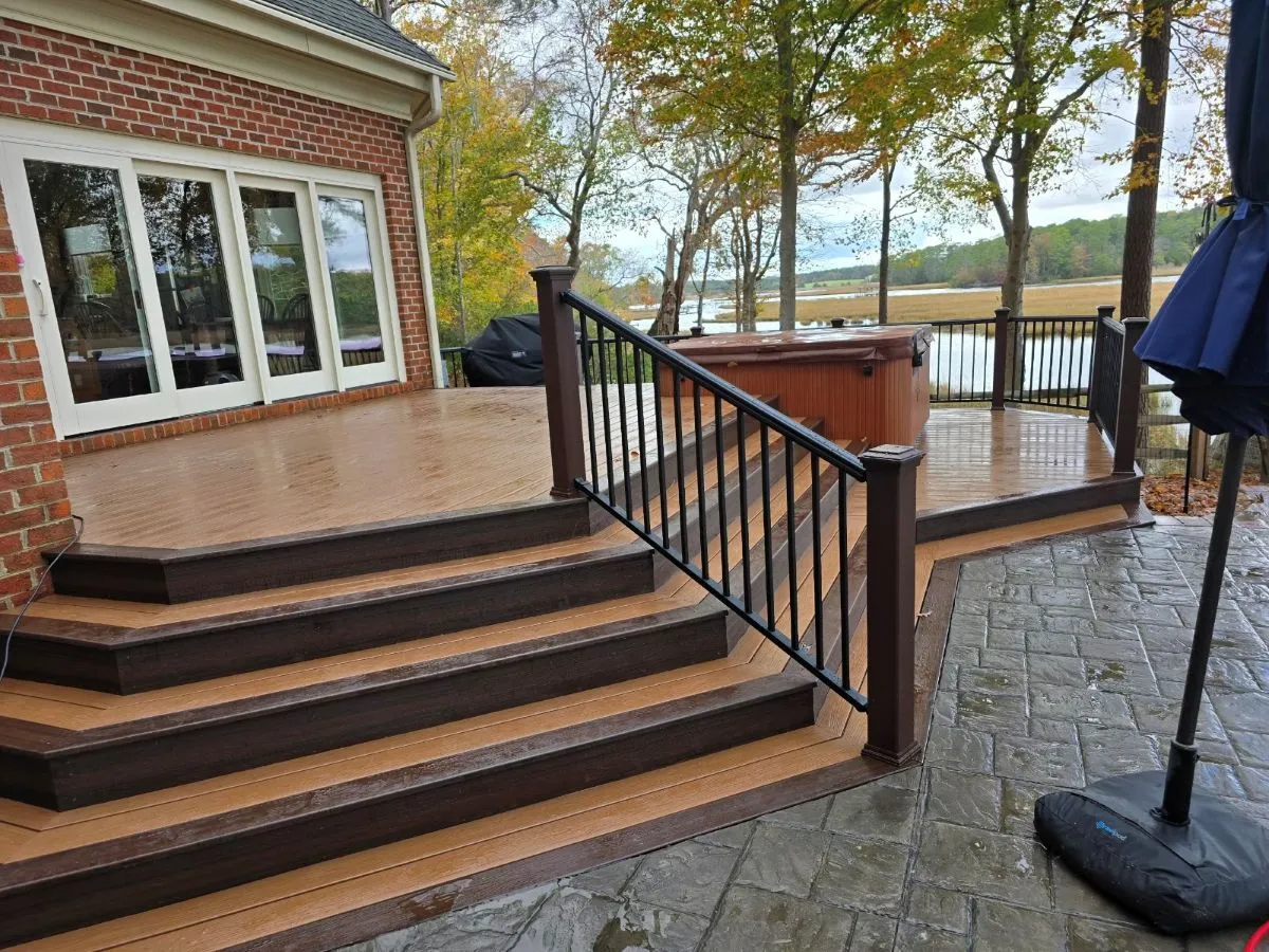 Dark brown composite deck with curved steps and black railings, next to a brick home with hot tub