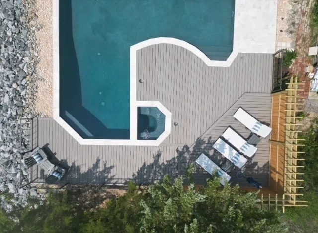 Custom poolside composite deck with curved edge and lounge chairs in a luxury backyard setting