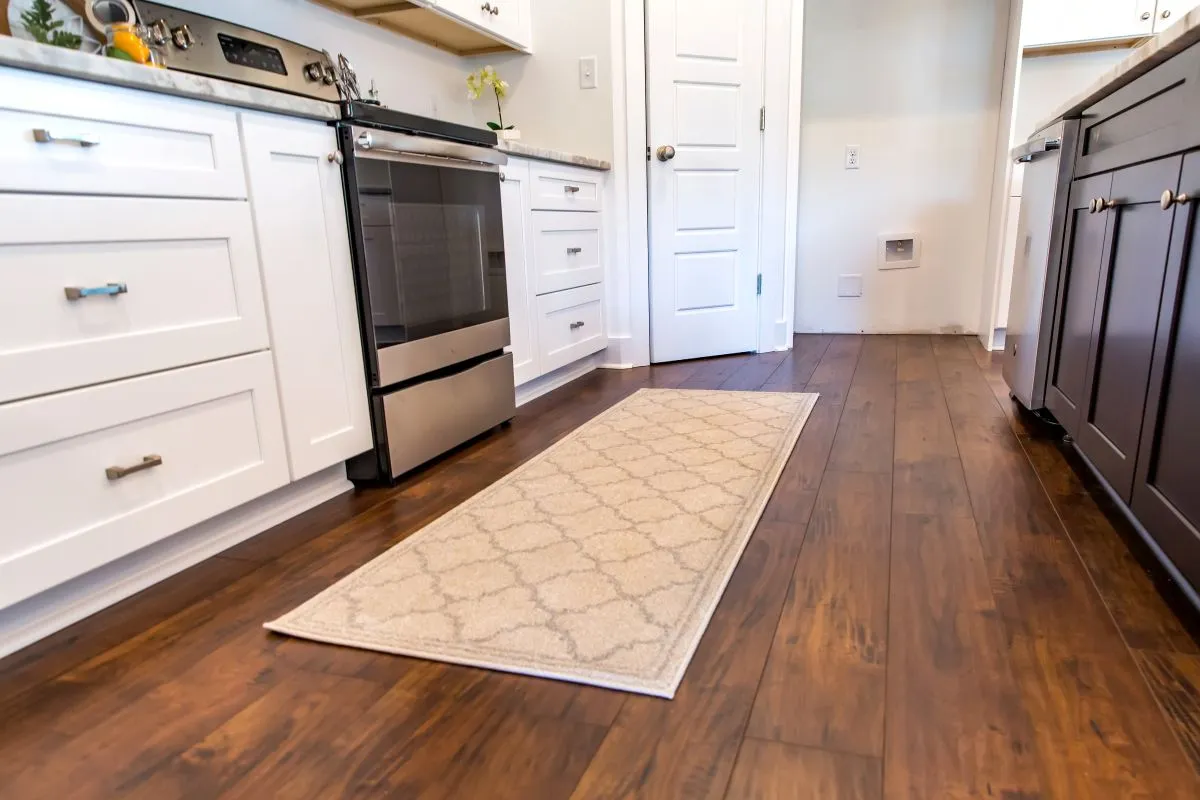 Hardwood floors in an open-concept kitchen with white cabinetry and a patterned runner