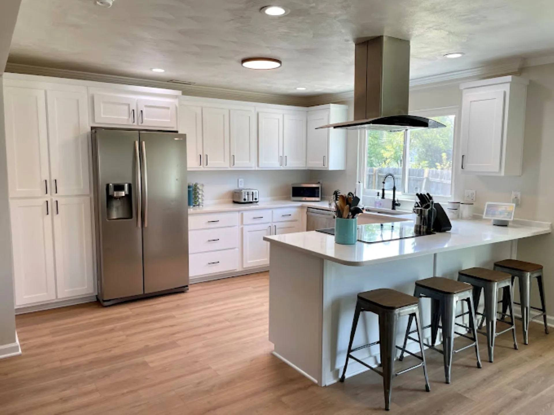 Open-concept kitchen with island seating, white shaker cabinets, and stainless steel fridge