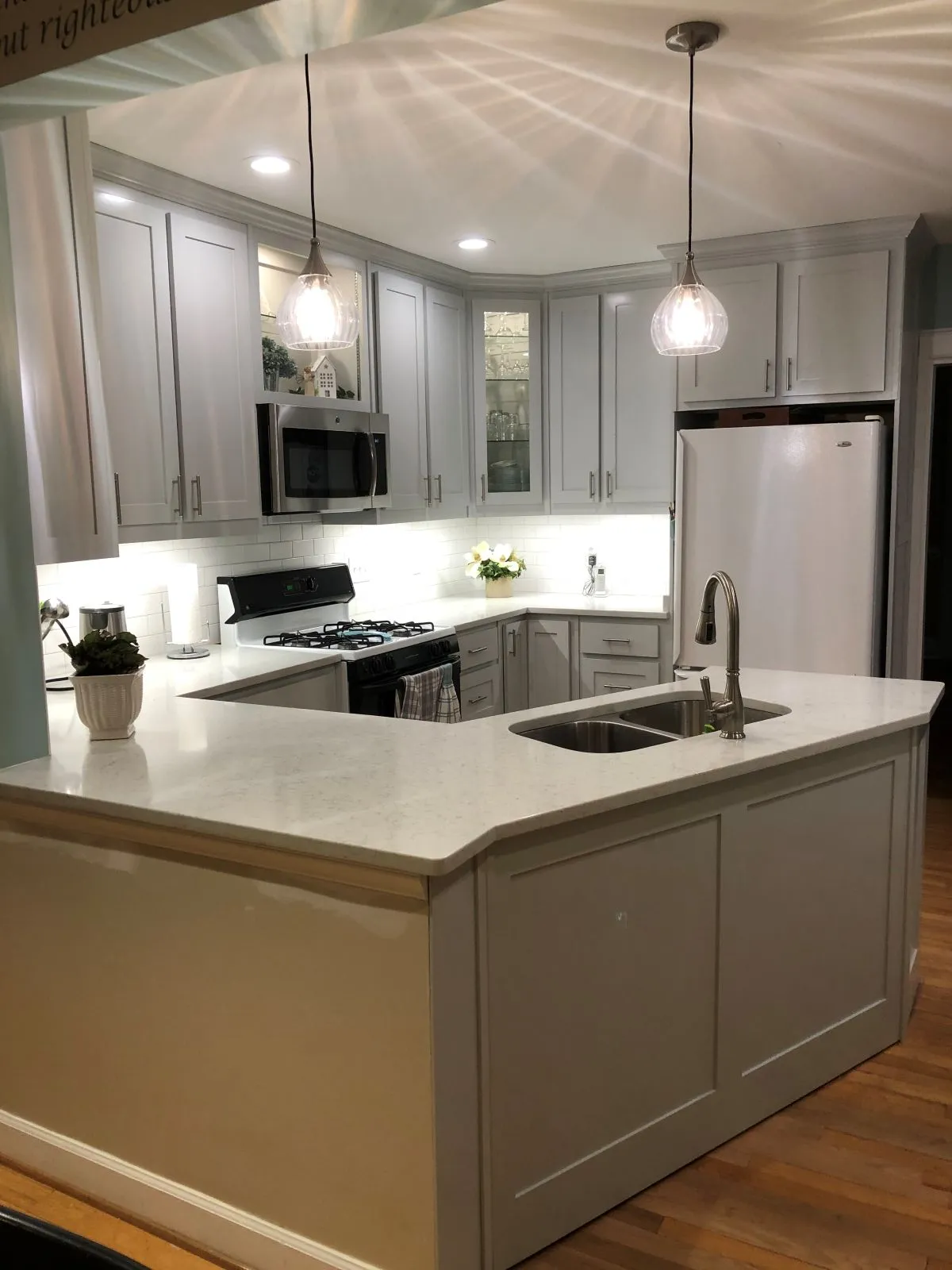 U-shaped kitchen with pendant lighting, central island sink, and glass cabinet display