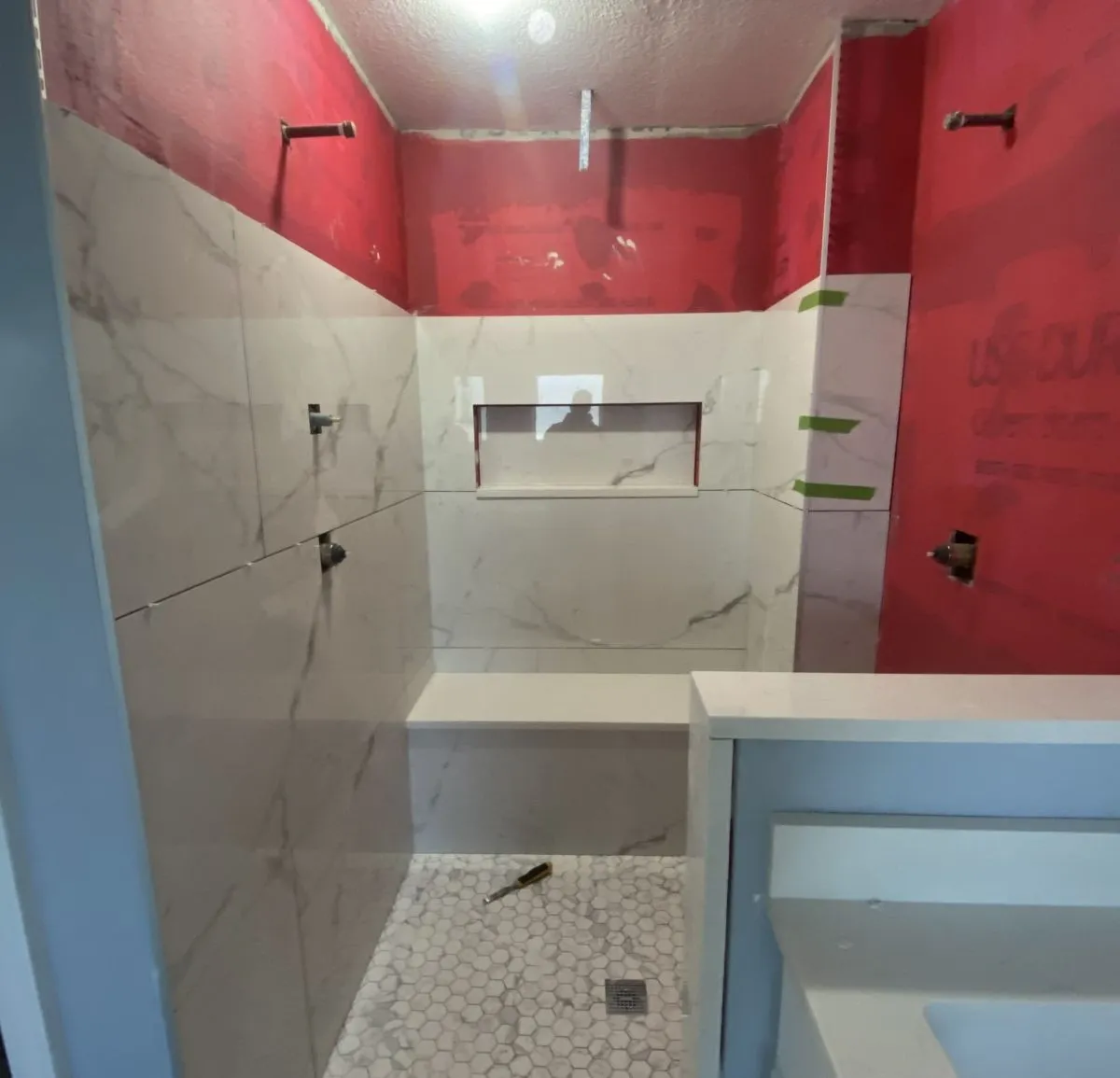 Tiled shower stall mid-rebuild with waterproofing membrane and new wall tile.