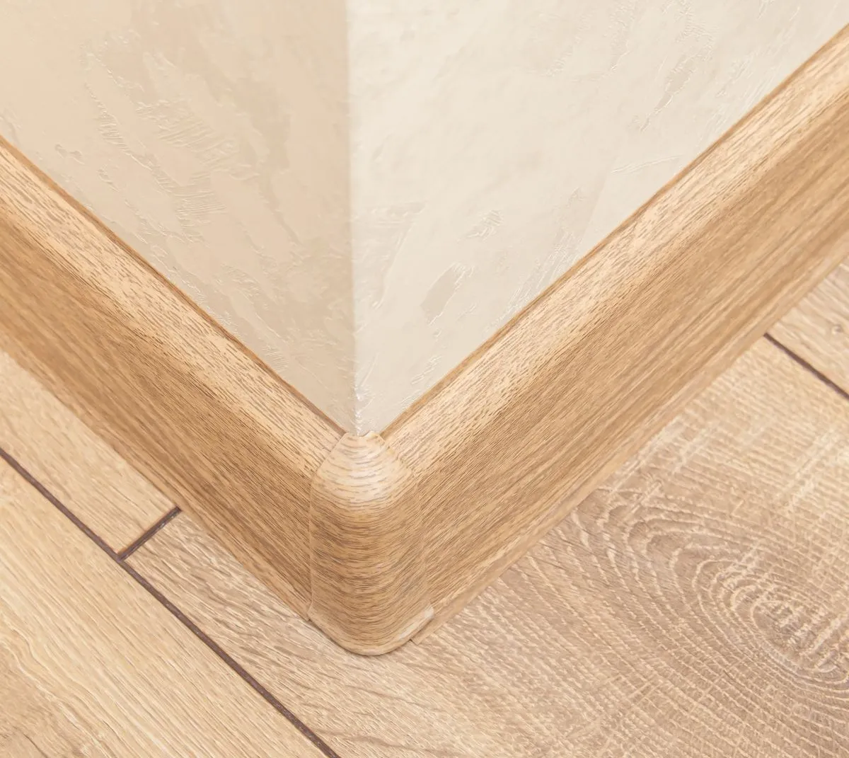 Tight corner detail of oak baseboard trim and matching wood plank flooring in a finished room