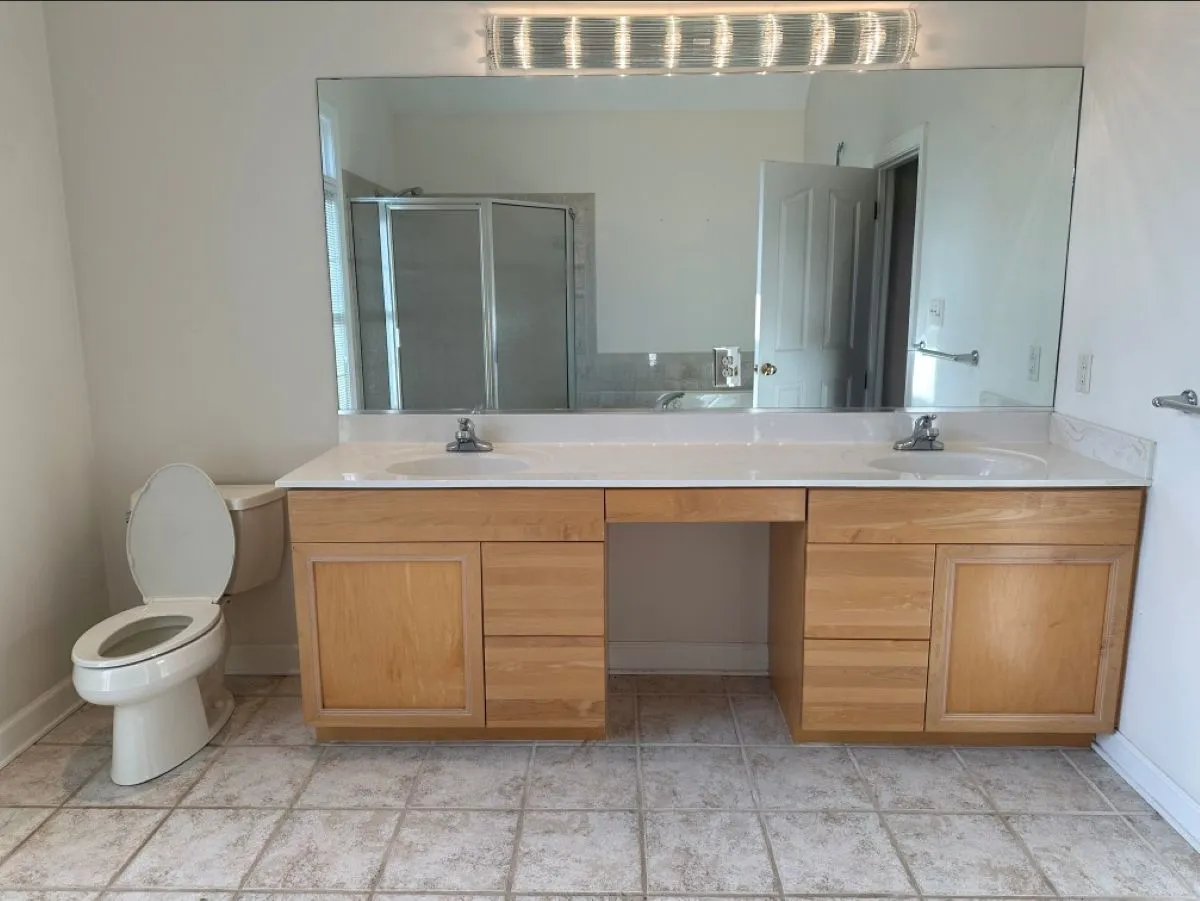 Before: builder-grade double vanity with wood doors and no backsplash in Virginia Beach bathroom