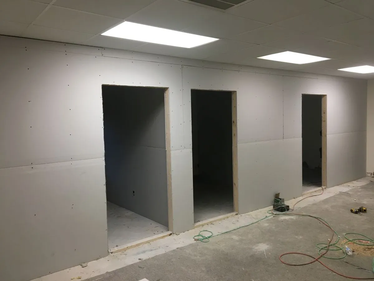 Drywall installed over framed office walls with door cutouts and recessed lighting